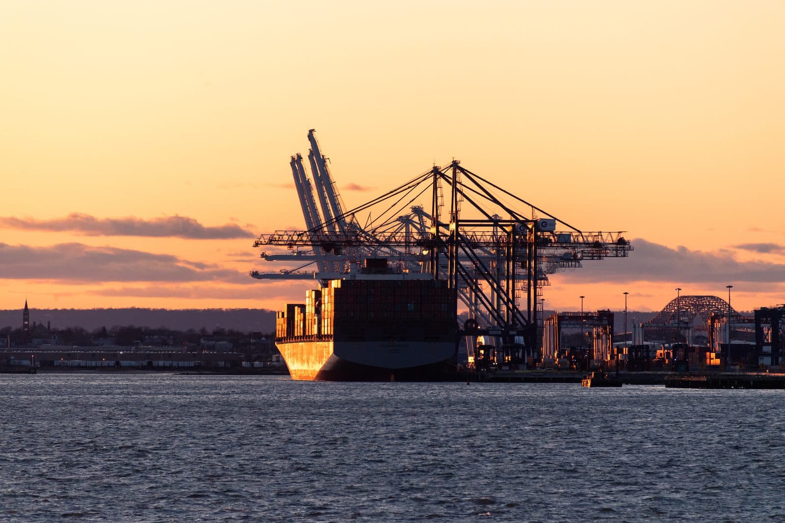 A container ship being loaded by cranes at a port terminal at sunset
